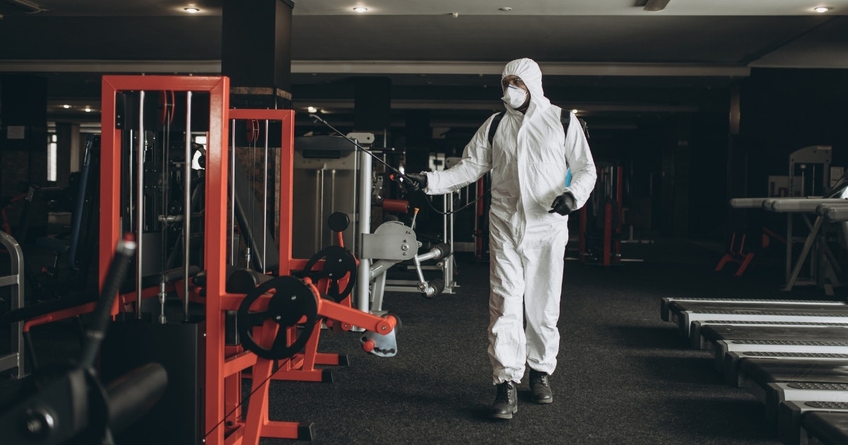 A man in a protective suit cleans a gym with chemicals